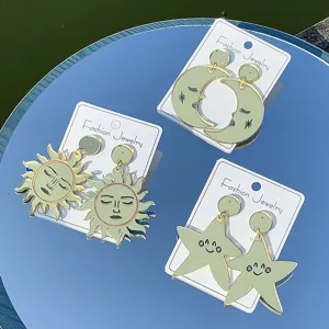 Detalle de pendientes de acrílico con diseño de sol, luna y estrella, bordes dorados.