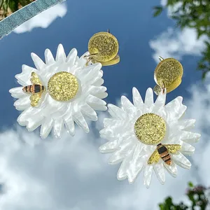 Nahaufnahme handgemachter Acryl Gänseblümchen Ohrringe mit glitzernden Bienen Details.