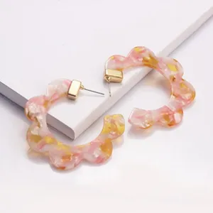 Nahaufnahme Detail modischer rosa floraler Acryl C-Creolen mit goldfarbenem Metallverbinder.