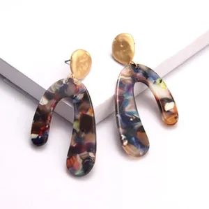 Nahaufnahme von abstrakten U-förmigen Acetat- und Gold-Statement-Ohrringen im Detail.