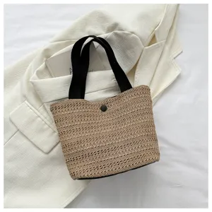 Detail view of woven straw bucket bag with black handles and secure button closure.