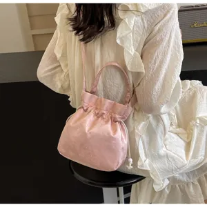 Dettaglio borsa a secchiello in satin rosa, design elegante a mano e tracolla per uso quotidiano.