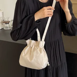 Chic borsa a secchiello in tessuto beige con coulisse indossata dalla modella, tracolla