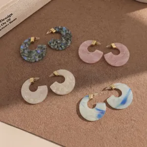 Close-up shot of colorful C-shaped acetate earrings featuring gold connectors on textured display.