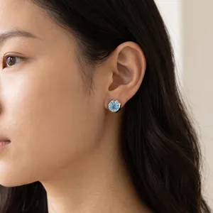 Close-up detail shot of exquisite floral stud earrings featuring a sparkling light blue gemstone worn on ear.