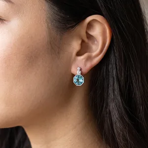 Close-up detail shot of elegant octagonal light blue gemstone earrings worn on ear.
