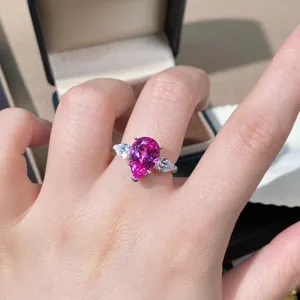 Close-up van een zilveren ring met roze saffier in peervorm en twee stenen ernaast.