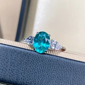 Primer plano de un brillante anillo ovalado de topacio Paraiba con piedras laterales y plata.