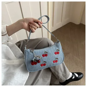 Chic denim shoulder bag featuring cute cherry embroidery and a metal cherry pendant accessory.