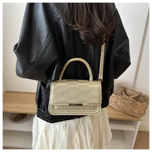 Vue détaillée d'un sac à bandoulière doré texturé à motif carreaux porté par un modèle.