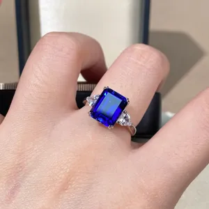 Primo piano di anello con gemma blu reale taglio smeraldo in argento con pietre laterali.