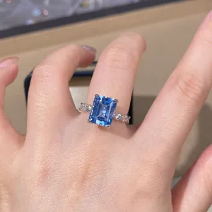 Close-up of emerald cut blue gemstone ring with pave side stones on sterling silver band.