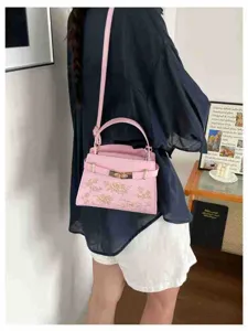 Pink shoulder handbag close-up showcasing detailed golden embroidery and metal lock.