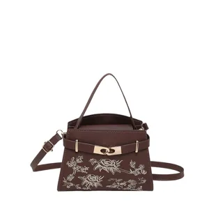 Elegant brown top-handle handbag with floral embroidery and classic metal lock strap.
