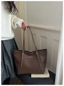 Primer plano del bolso tote de cuero trenzado marrón oscuro con textura fina y herrajes.