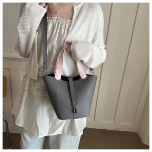 Close-up detail of stylish grey bucket bag with contrast pink top handles and padlock.