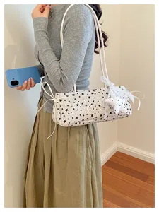 Primo piano dettagliato di una elegante borsa a spalla bianca con stampa stelle nere e fiocchi.