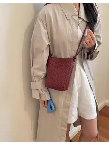 Detailed view of a stylish woven crossbody bag worn with a chic trench coat in daily scene.