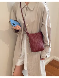 Detail shot of dark red woven leather crossbody phone bag, paired with a casual outfit.
