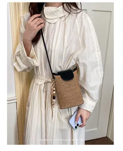 Detalle de bolso cruzado de paja trenzada retro, solapa negra elegante y colgante de borla.