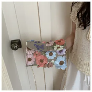Detail view of stylish embroidered floral shoulder bag with delicate metallic chain strap design.