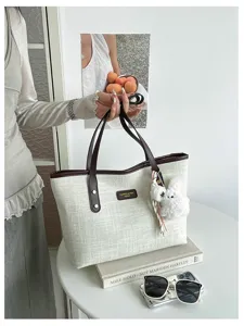 Textured canvas tote bag detail featuring a cute plush bunny charm and brown leather trim.