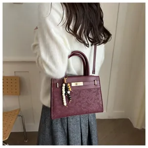 Detailaufnahme der bordeauxroten Handtasche aus Prägeleder mit edlem Perlenanhänger.
