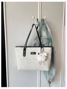 Chic canvas tote bag with black handles and cute plush charm, perfect for daily commuting.