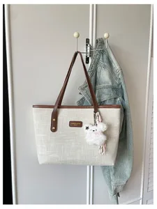 Detail view of a stylish beige canvas tote bag with brown leather handles and cute plush bear charm.