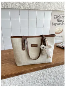 Beige canvas tote bag detail, brown leather handles, cute plush bear charm, casual style.