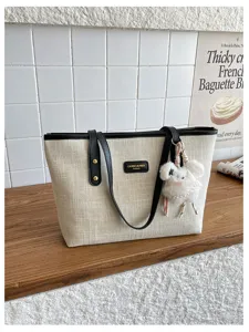 Detailed shot of a beige canvas tote bag with black leather handles and cute plush charm.