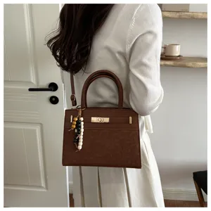 Detailaufnahme der braunen Lederhandtasche mit Metallverschluss und stilvollen Perlen.