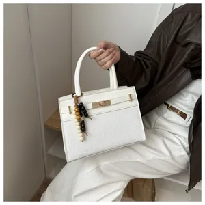 Weißes Handtaschen-Detail mit strukturiertem Design, Metall-Drehverschluss und Perlenanhänger.