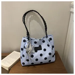 Dettaglio borsa a tracolla in tela a pois, con manici intrecciati neri e ciondolo a stella.