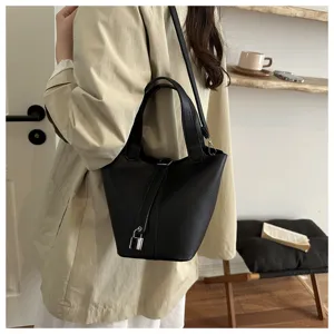 Detail shot of a chic black leather bucket bag worn by model, featuring silver padlock.
