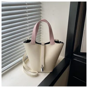 Detail shot of chic cream bucket bag with pink handles, minimalist lock design and shoulder strap.