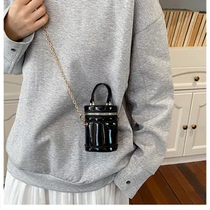 Petit sac seau cylindrique en cuir verni noir avec bandoulière chaîne et détails cloutés chics.