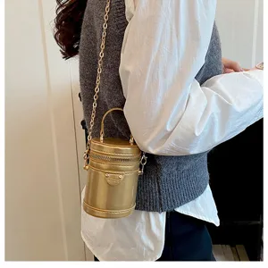 Vue détail d'un sac seau cylindrique doré métallisé avec bandoulière chaîne porté.