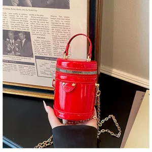 Détail de mini sac cylindre en cuir vernis rouge, poignée élégante et bandoulière chaîne femmes.