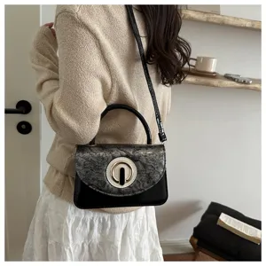 Detailed view of trendy small black square handbag featuring snake pattern flap and gold ring clasp.