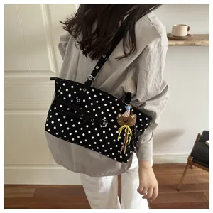 Primo piano della borsa a spalla a pois neri e bianchi con ciondolo a forma di orsetto.