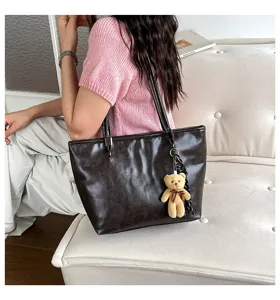 Vista dettagliata della borsa tote in pelle marrone scuro con ciondolo orsetto per lavoro.