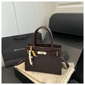 Braunes Damen Handtaschen Detail mit goldenem Drehverschluss und dekorativem Perlenanhänger.