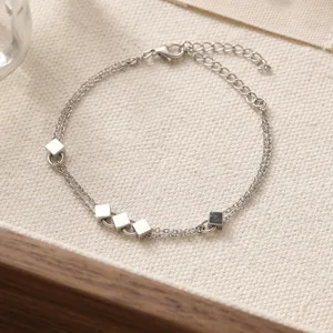 Close-up detail of silver double layer bracelet with small cube charms on textured fabric.