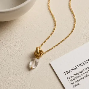 Detailed shot of gold chain necklace with textured knot pendant and clear crystal drop.