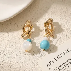 Close-up shot of trendy metal knot earrings with pearl and turquoise beads on textured background.