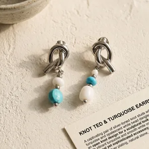 Detail view of silver-toned knot earrings featuring turquoise and white bead dangles.