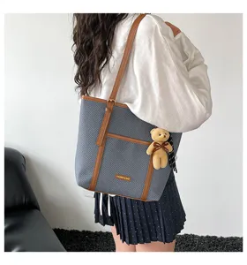 Close-up of blue textured tote bag with brown straps and cute bear pendant detail.