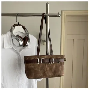 Detalle de bolso de hombro retro marrón con elegante hebilla de cinturón y anillos metálicos.