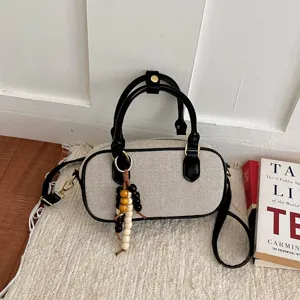 Bolso de hombro bowling de lona beige, ribete de cuero negro y dije de cuentas de madera.